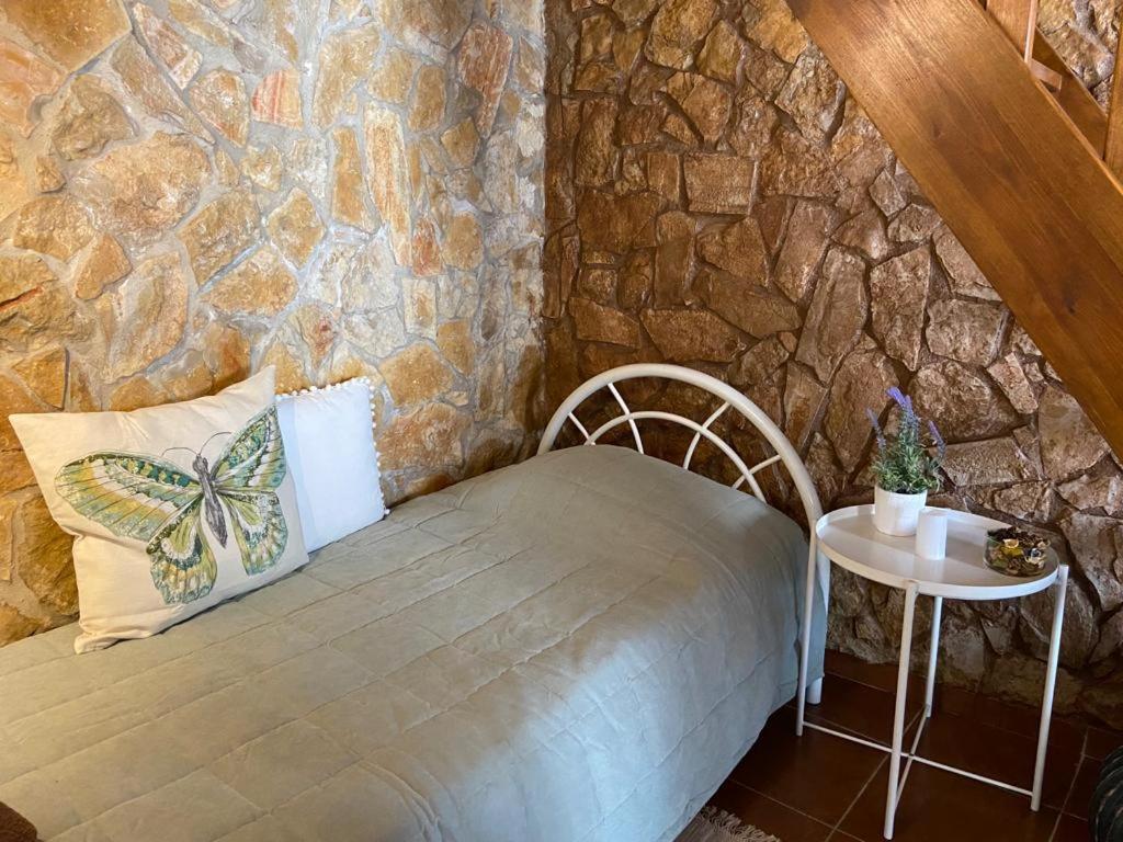 Habitación con paredes de piedra, cama y mesa. en Casa Alfarroba en Barão de São Miguel