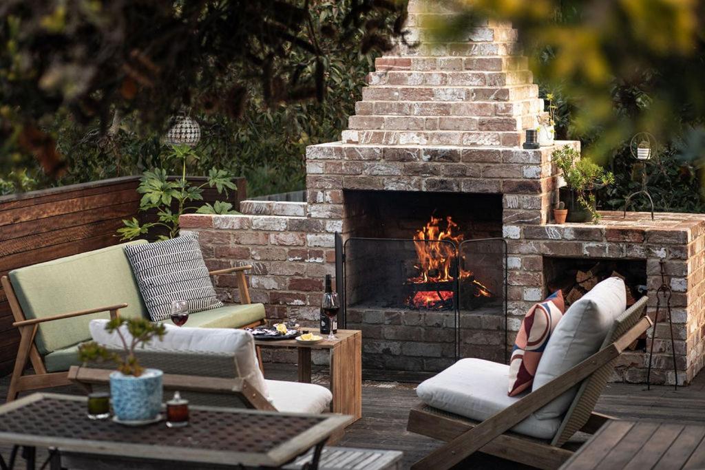 a patio with a brick fireplace with chairs and a table at Driftwood Rest Binalong Bay Sleeps 4 in Binalong Bay