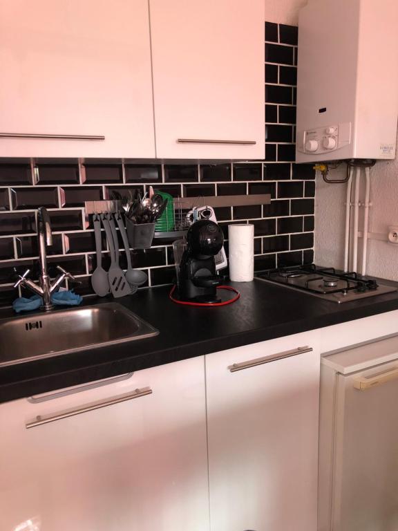 - une cuisine avec un évier et un mur en carrelage noir dans l'établissement location studio 4 pers piscine, au Cap d'Agde