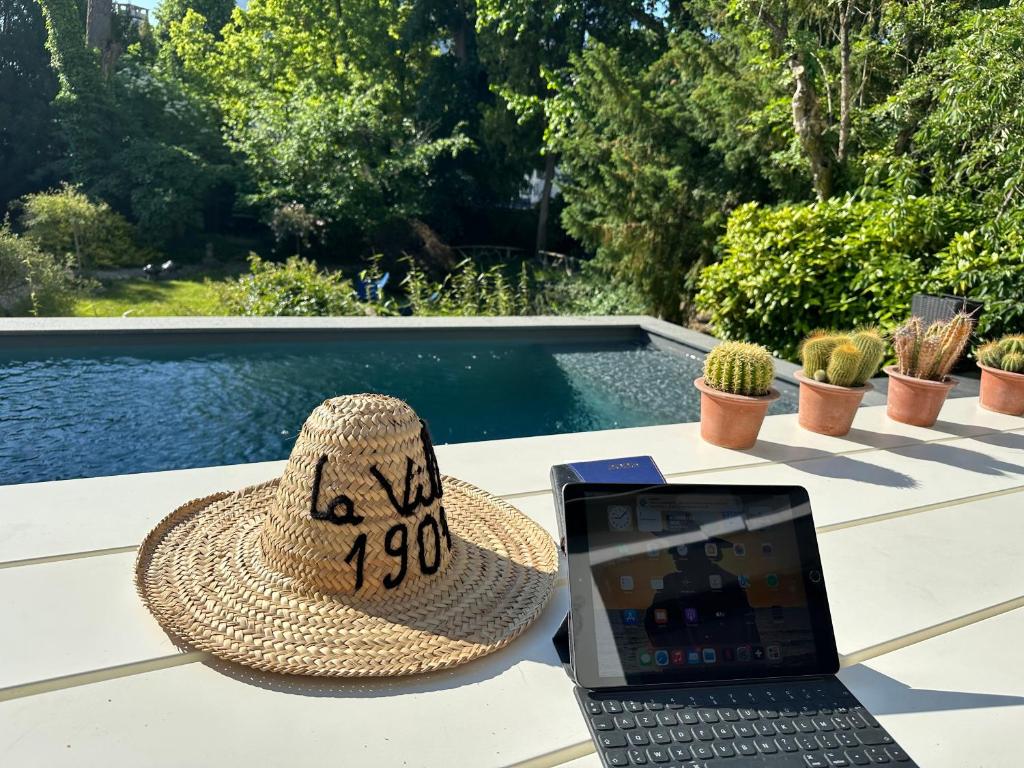 a straw hat and a laptop sitting on a table next to a swimming pool at La Villa 1901 in Nancy