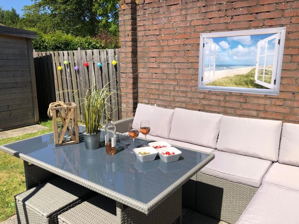 a patio table with a white couch and a window at Comfortabel 6-persoons huisje nabij strand, bos, duinen en stad in Warmenhuizen