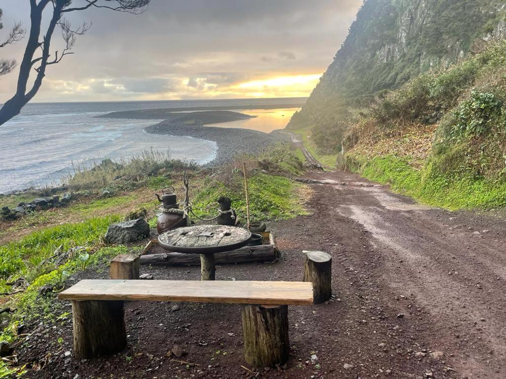 a bench on a dirt road next to the ocean at Kuanza Nature Experience, Fajã do Belo in Fajã da Caldeira de Santo Cristo