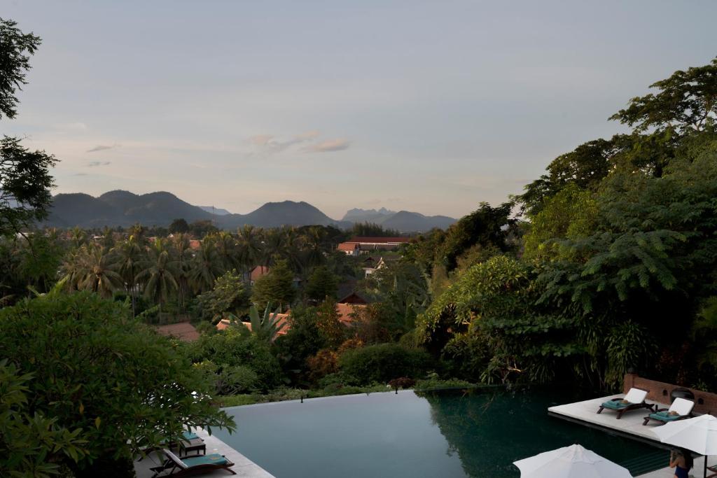 a swimming pool in a garden with mountains in the background at La Résidence Phou Vao, A Belmond Hotel, Luang Prabang in Luang Prabang