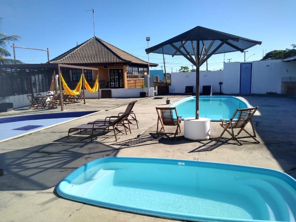 a swimming pool with chairs and an umbrella at Villaggio dos Ventos in Arraial do Cabo