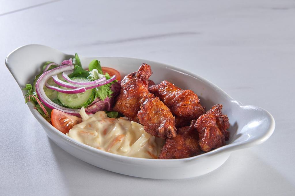 a white bowl of food with chicken wings and salad at The Crown Hotel in Weymouth