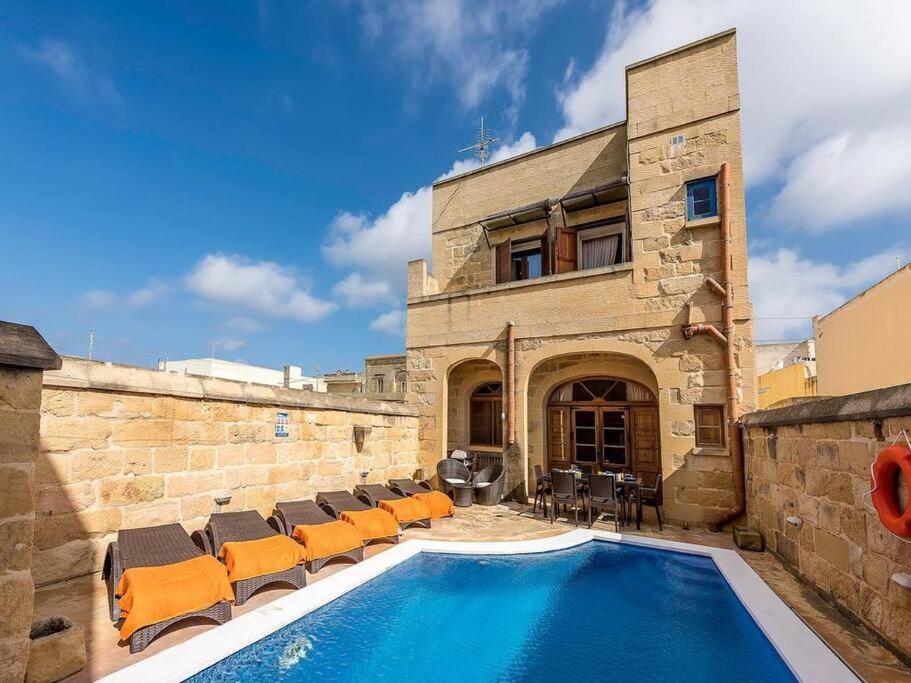 a swimming pool with chairs and a building at Traditional farmhouse with pool in Xagħra