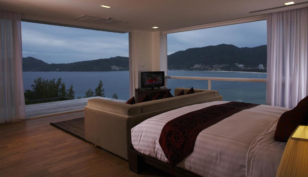 a bedroom with a bed and a couch and large windows at Jirana Patong in Patong Beach