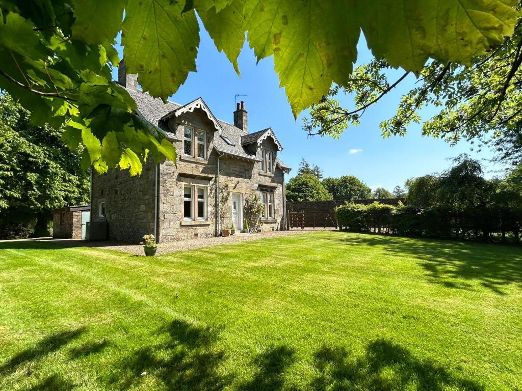 Luxury Garden Cottage في Dalry: منزل حجري قديم مع ساحة عشبية كبيرة