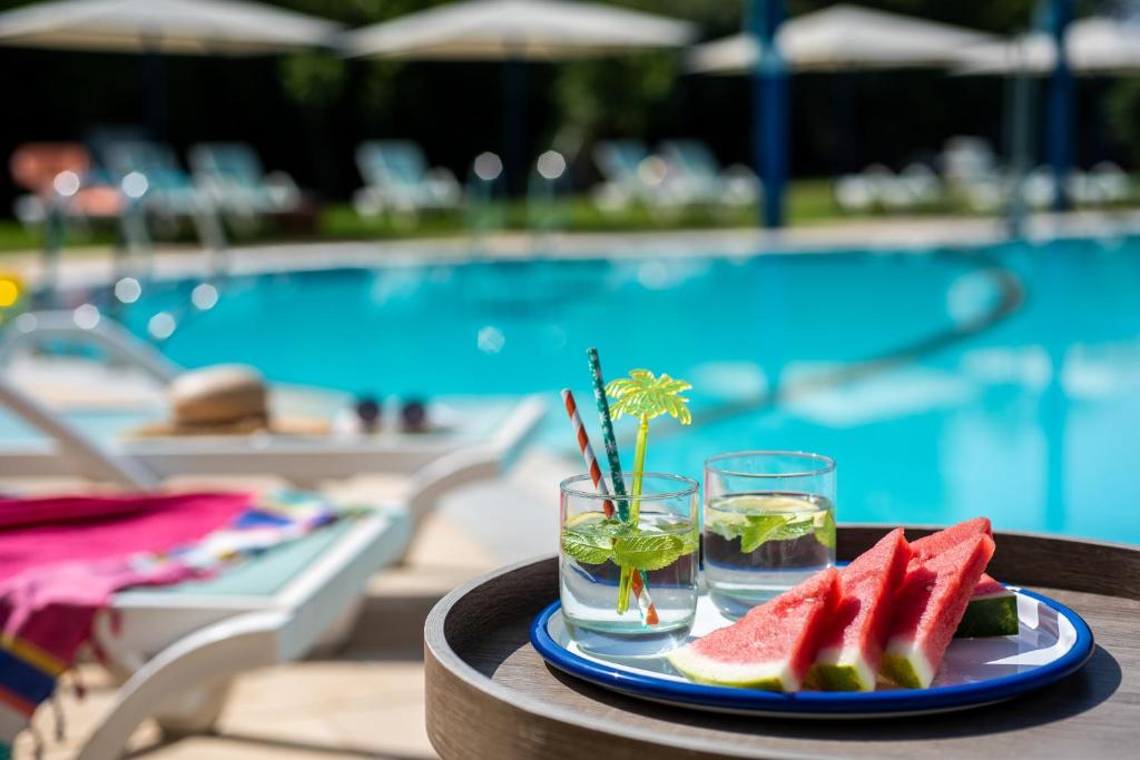 um prato de melancia e bebidas numa mesa perto de uma piscina em The Village- Jordan Riverside Travel Hotel em Sede Neẖemya