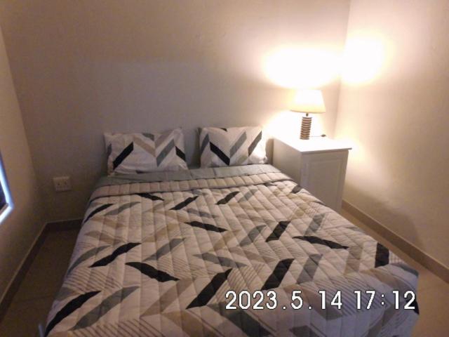 1 dormitorio con 1 cama con edredón y lámpara en The Cottage en Krugersdorp