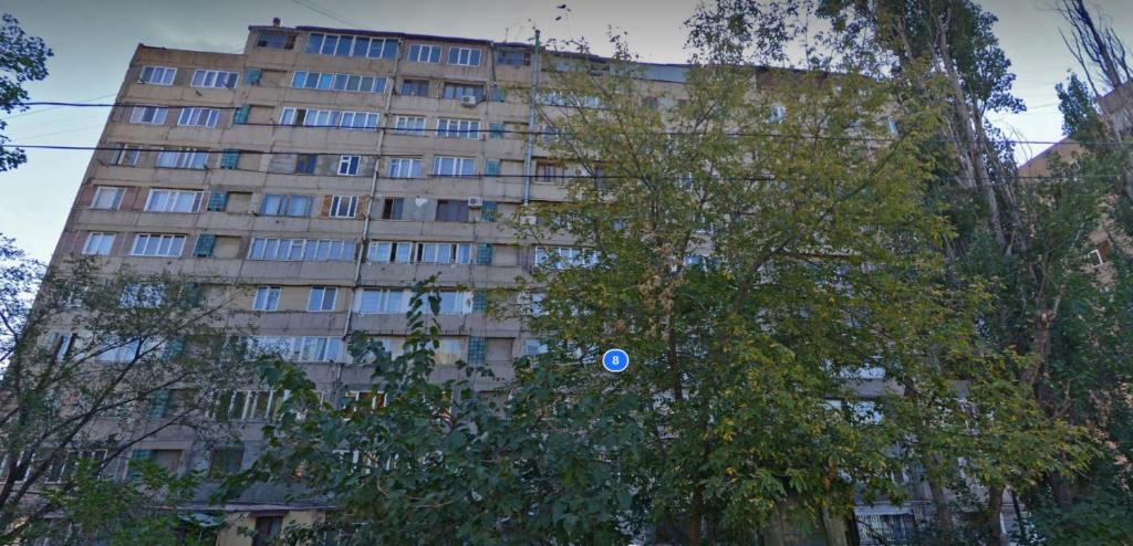 a tall building with a blue sign in front of a tree at Avchieva's apartment on Orbeli Brothers Street in Yerevan