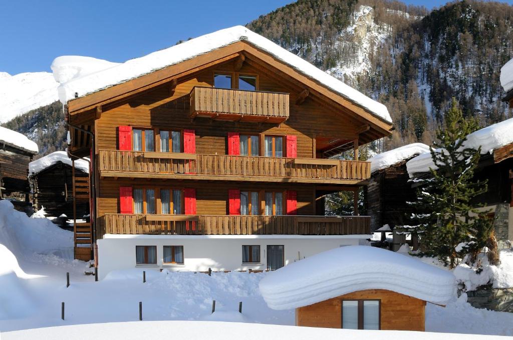 ein Blockhaus im Schnee mit roten Fenstern in der Unterkunft Haus Leopold in Zermatt