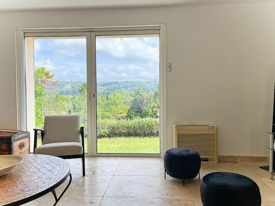 a living room with a table and chairs and a large window at Belle villa avec jardin piscine et salle de sport in Montauroux