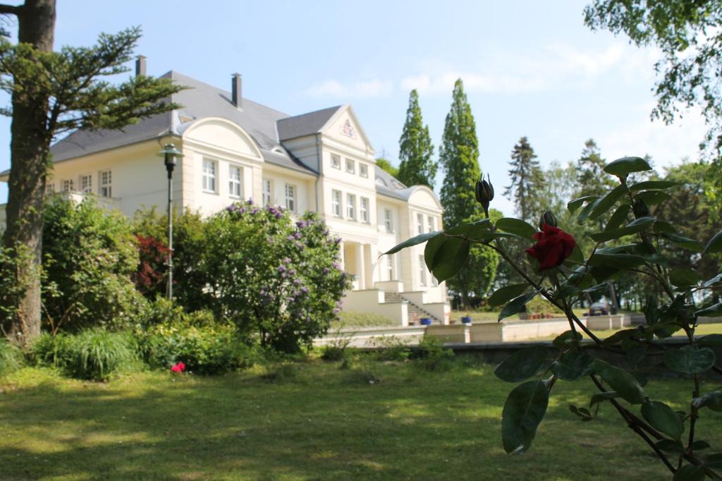 une grande maison blanche avec une fleur rouge dans la cour dans l'établissement Schloß Wichmannsdorf, à Kröpelin