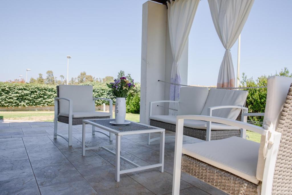 un patio con 2 sillas blancas y una mesa en Le Residenze di Baia Sant'Anna en Tanaunella