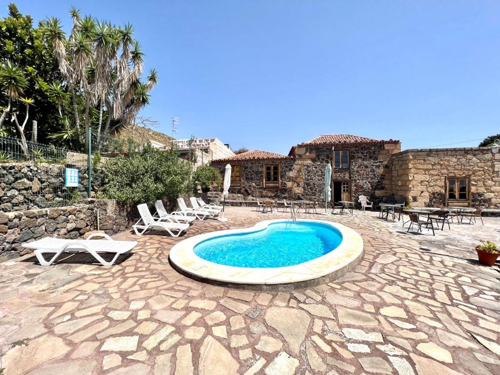 a swimming pool in a patio with chairs and a house at Apto en caserío rural con cocina, piscina, Wifi, barbacoa y jardín compartidos in San Miguel de Abona