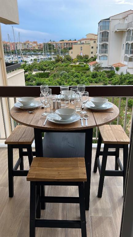 einen Holztisch mit Gläsern und Tellern auf dem Balkon in der Unterkunft Belle vue in Cap d'Agde