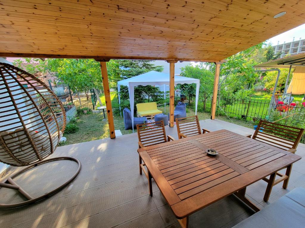 een veranda met een houten tafel en stoelen en een schommel bij Cozy villa, Golem beach. in Golem