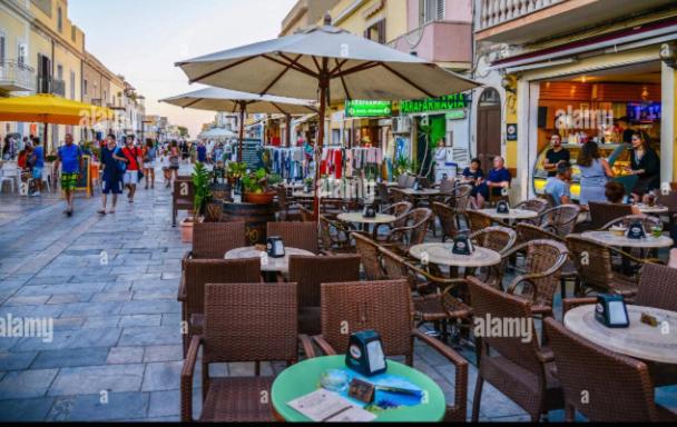 una cafetería al aire libre con mesas, sillas y sombrilla en La Perla di Lampedusa, en Lampedusa