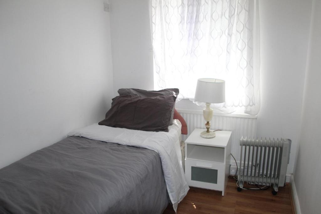 a bedroom with a bed and a lamp and a window at Cozy light single bedroom in Edgware