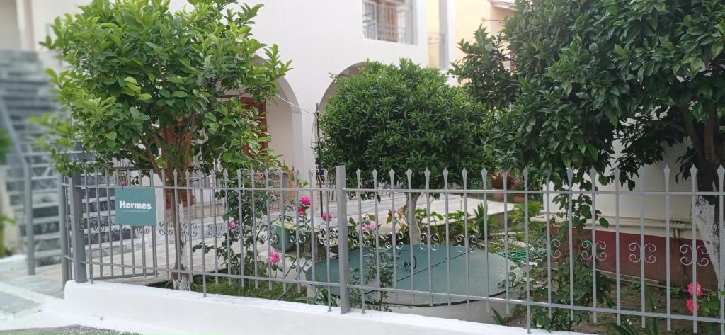 a fence with trees and flowers in front of a building at Hermes Comfort Apartment in Kavos