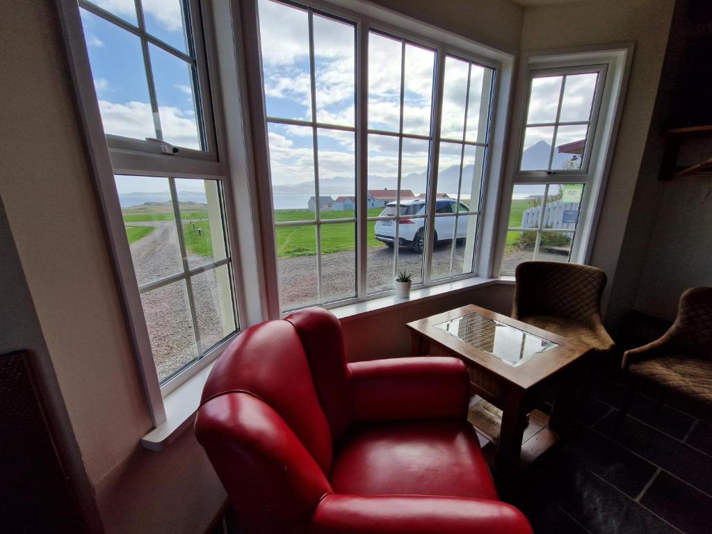 a living room with a red chair and a table and windows at Berunes HI Hostel in Berunes
