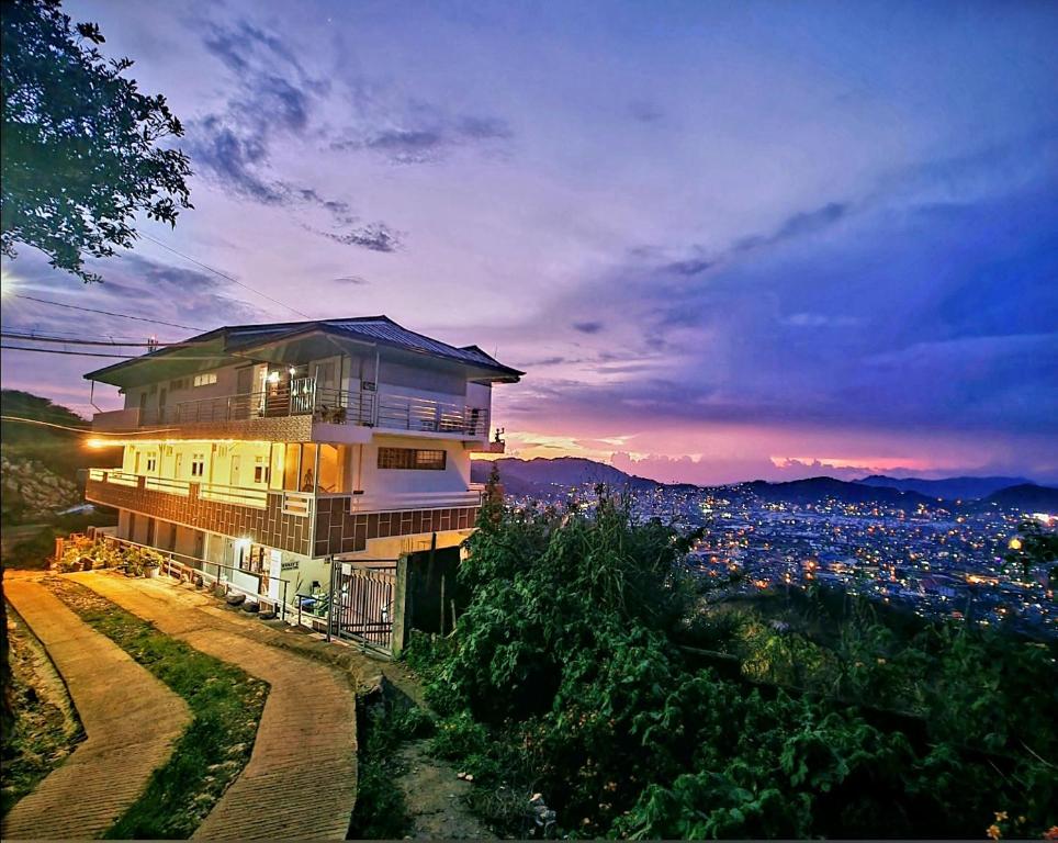 ein Gebäude auf einem Hügel mit einer Stadt im Hintergrund in der Unterkunft Wanay's Rocky Mountain Homestay in Baguio City