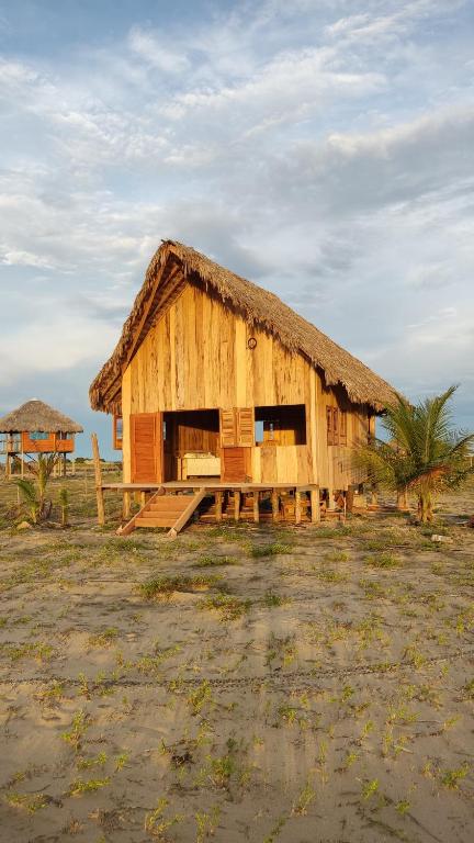 a wooden hut with a thatched roof in a field at Pousada Amor Do Arpoador in Tutóia