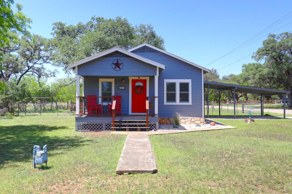 a small blue house with a red door in a yard at Bandera Bungalow - River, Downtown, Peaceful fenced corner lot! King bed! in Bandera