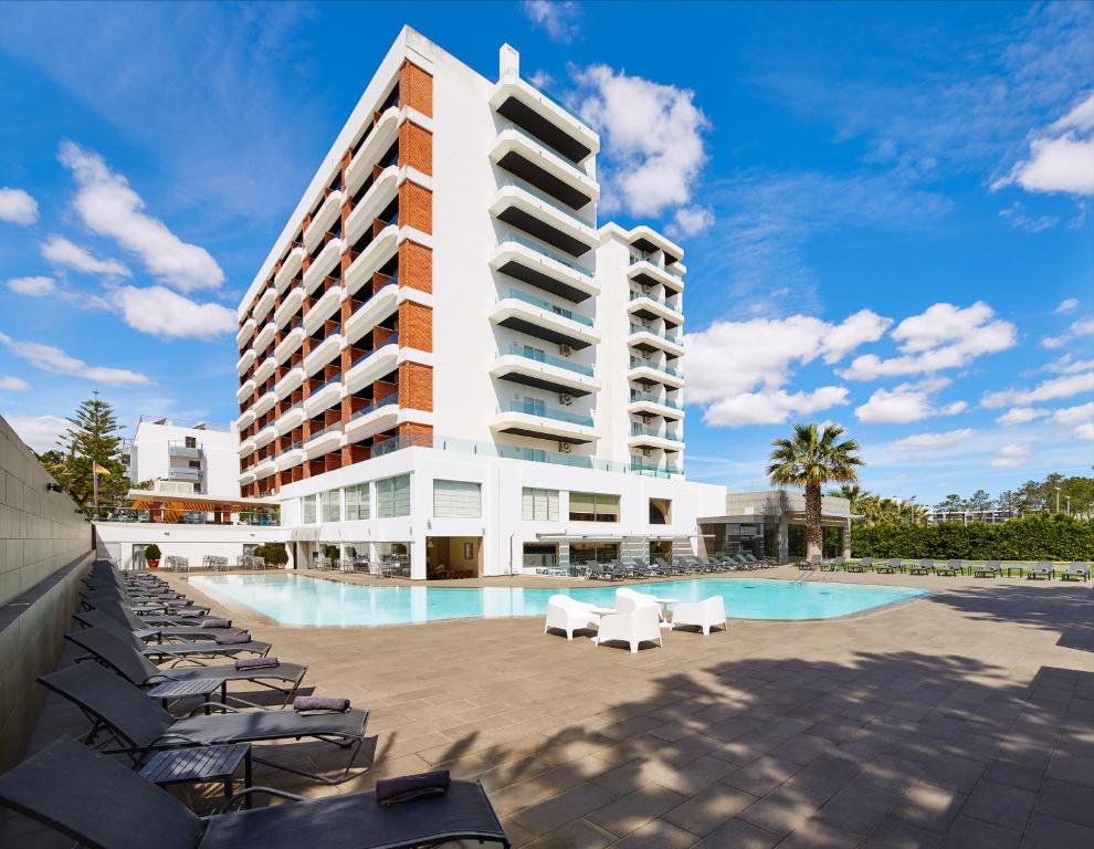 a hotel with a swimming pool and chairs and a building at Alcazar Hotel & SPA in Monte Gordo