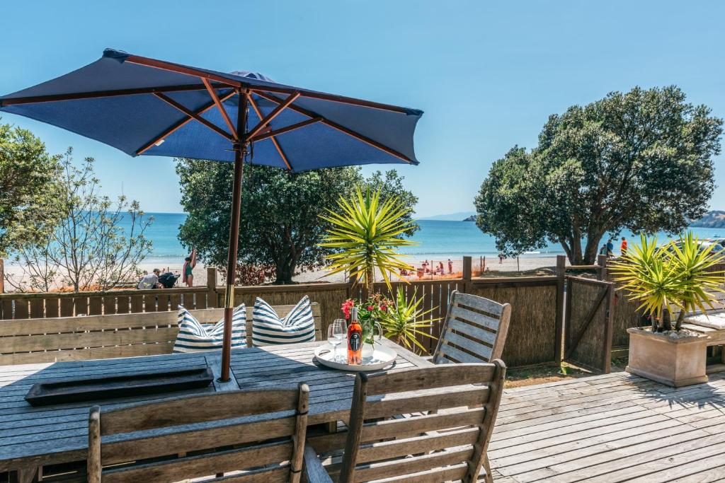 a table with an umbrella on a deck with the beach at Onetangi Waterfront Bach - Coast & Country in Onetangi