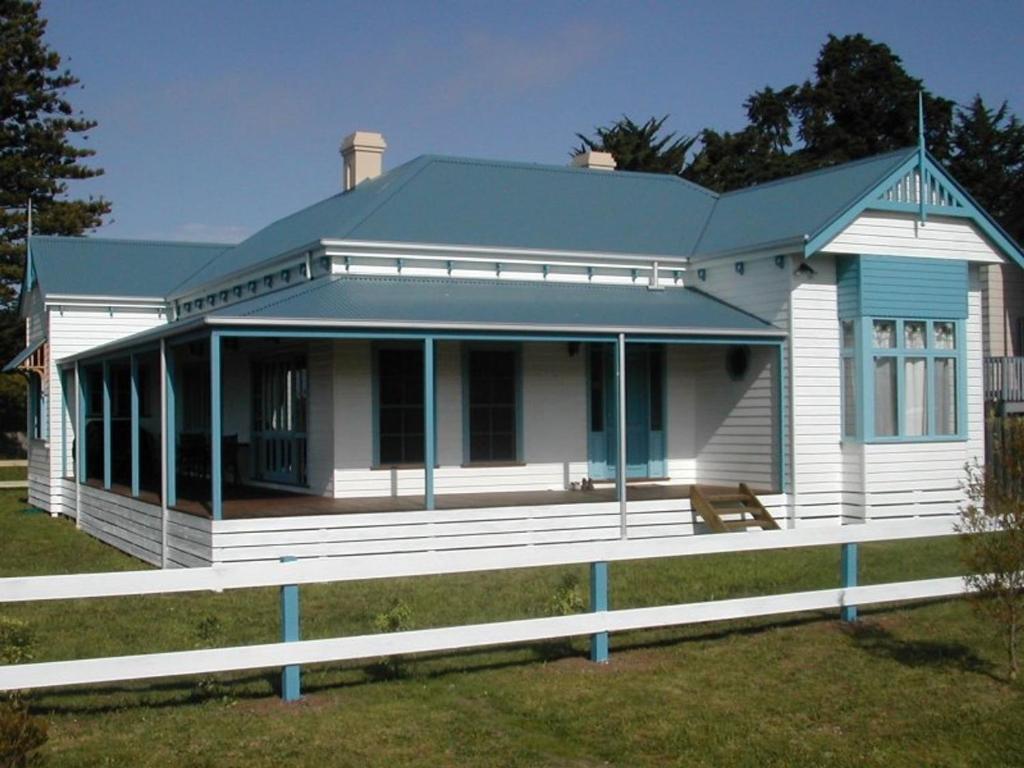 a white house with a blue roof on a field at Heritage Haven on Phillip Island in Cowes