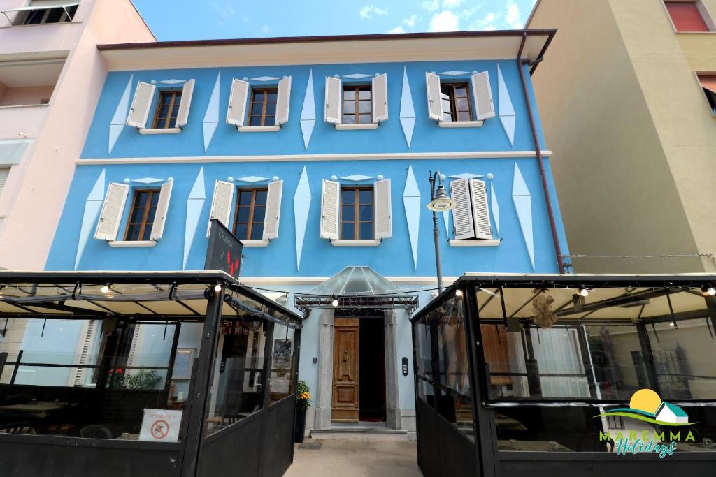 un bâtiment bleu avec des fenêtres blanches sur une rue dans l'établissement Maremma Holidays -Residenza Olesià, à Follonica