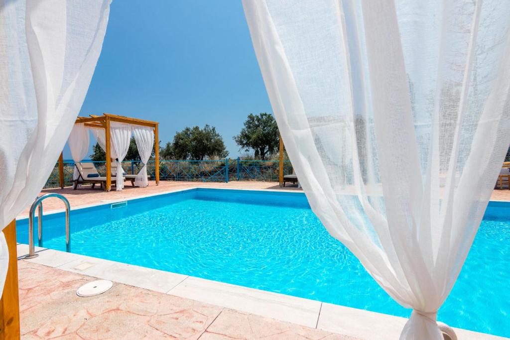 a swimming pool with blue water and white curtains at Koroni Xenios Zeus, Seaview Summer Retreats in Koroni