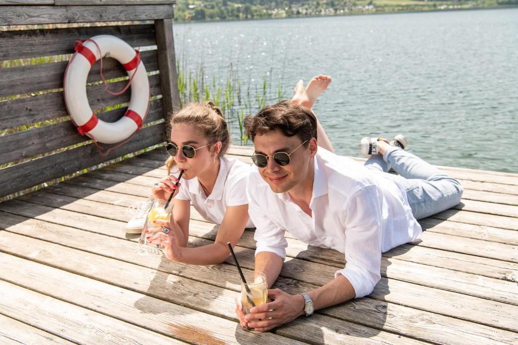 a man and woman laying on a dock with drinks at Seehotel Urban in Bodensdorf