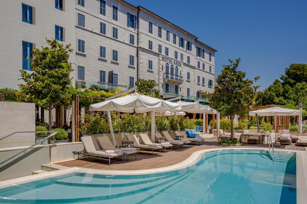 a pool with chairs and umbrellas next to a hotel at Hotel Park Split in Split