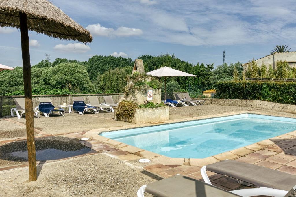 a swimming pool with chairs and an umbrella at La Masía Grande de Can Gat Vell in Llampaies