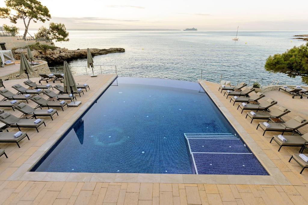 a swimming pool with chairs and the ocean in the background at Hospes Maricel y Spa, Palma de Mallorca, a Member of Design Hotels in Cas Catala