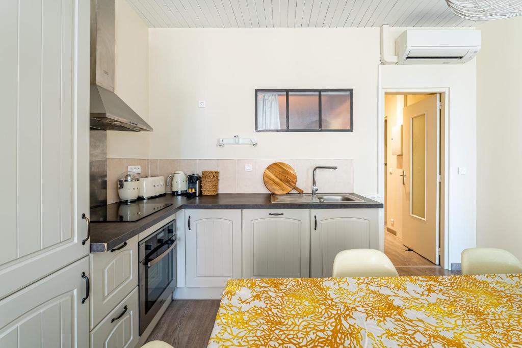 a kitchen with white cabinets and a sink and a table at Le Nani Raou par Dodo à Cassis in Cassis