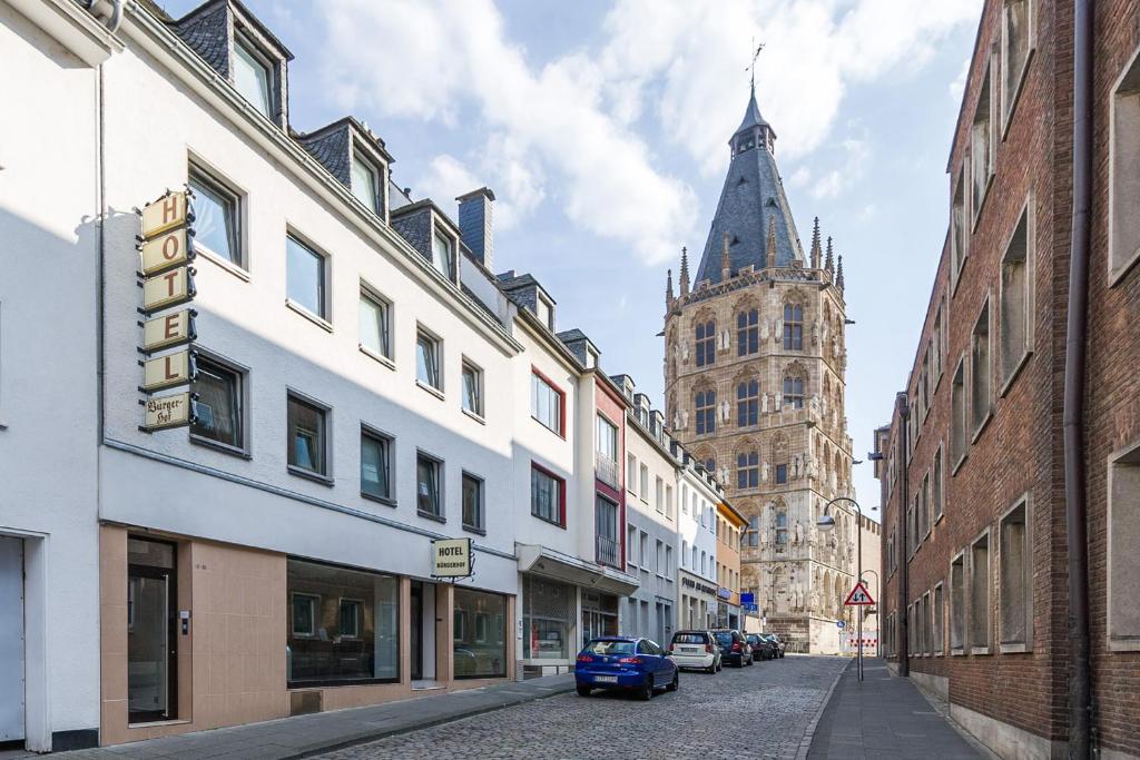 eine Stadtstraße mit Gebäuden und einem Uhrturm in der Unterkunft Bürgerhofhotel in Köln