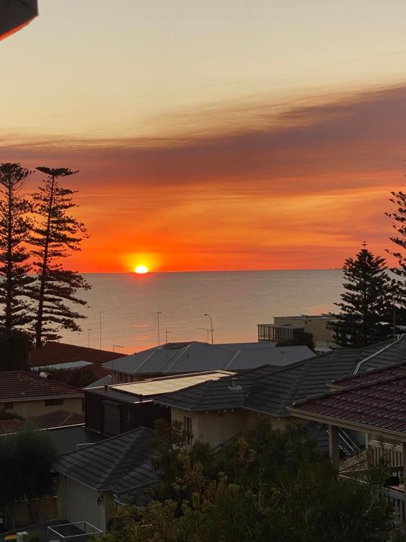 una puesta de sol sobre el océano y los tejados de las casas en Ocean Eye en Perth