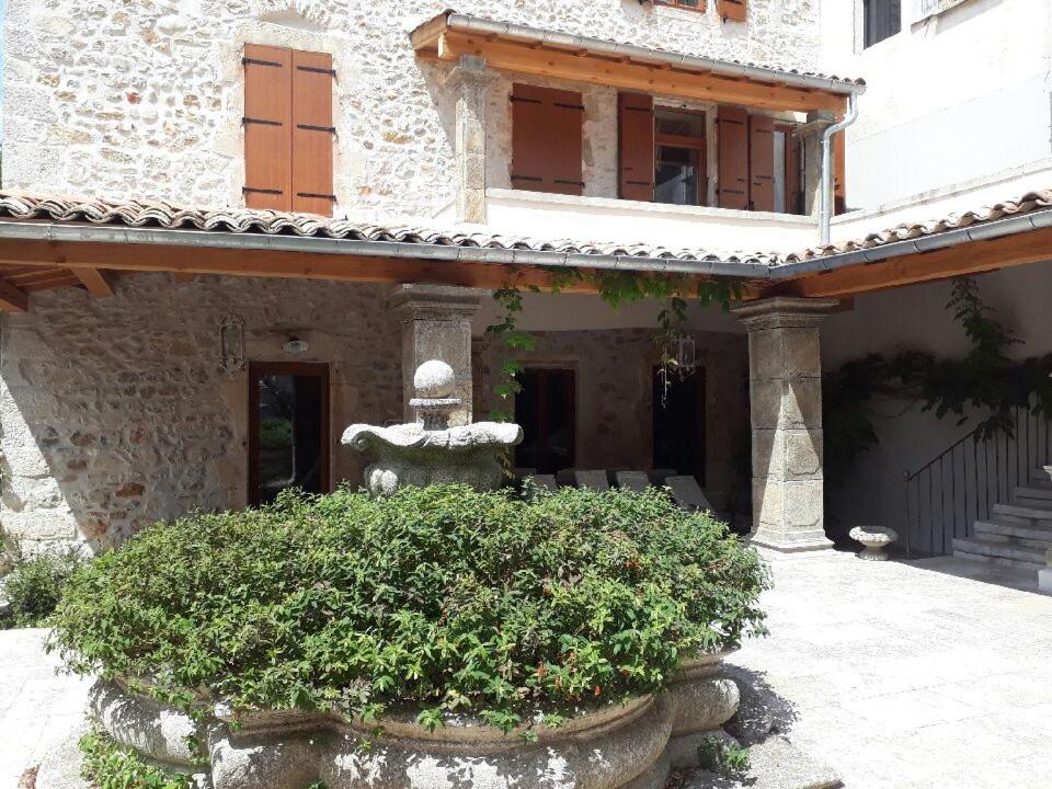 a stone building with a statue in front of a bush at Le Préau in Vallon-Pont-dʼArc