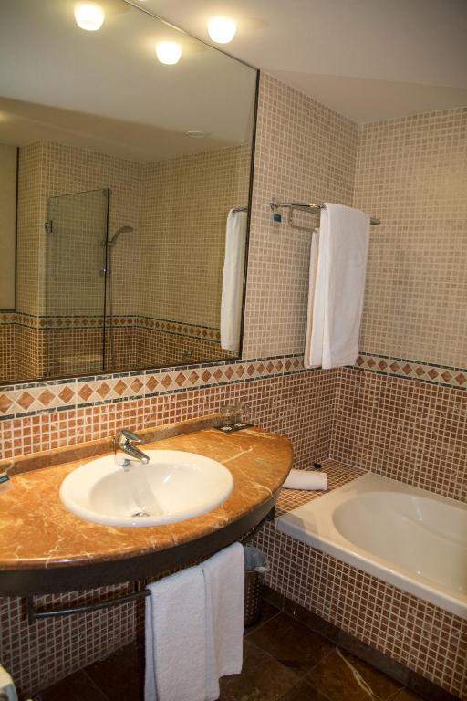 a bathroom with a sink and a tub and a mirror at Hotel Nuevo Portil Golf in El Rompido