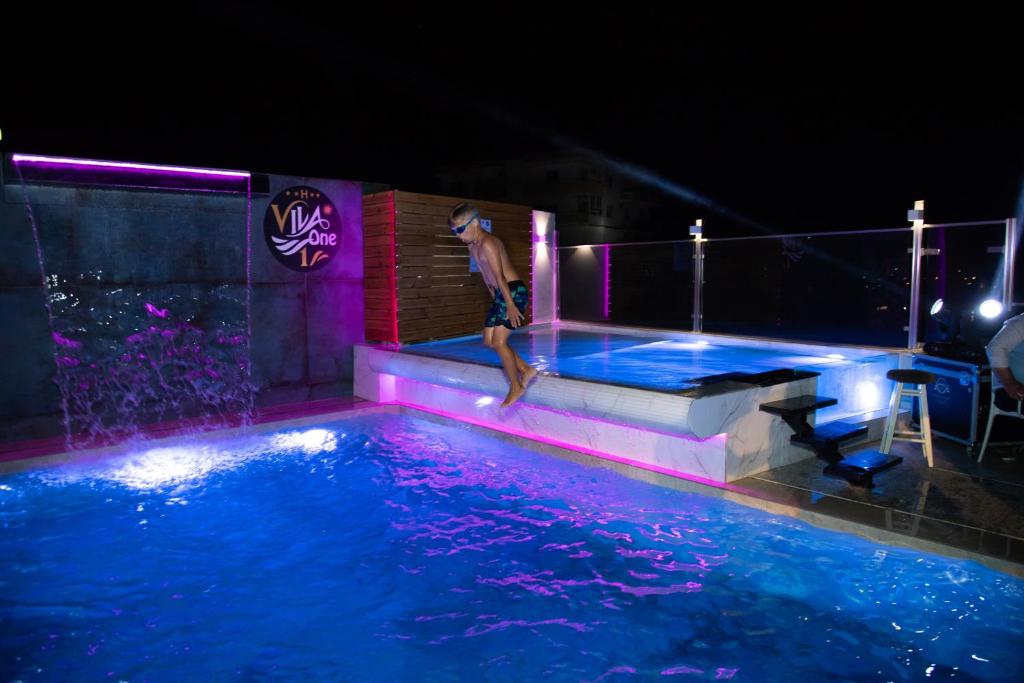 a man jumping into a swimming pool at night at Vila One Beach Hotel in Durrës
