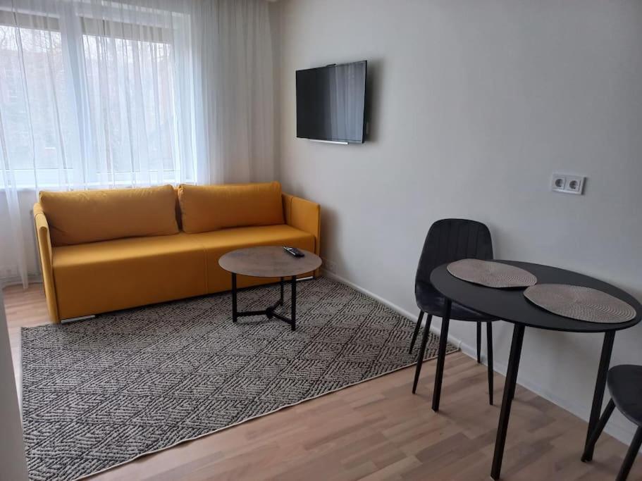 ein Wohnzimmer mit einem gelben Sofa und 2 Tischen in der Unterkunft City center apartment in Klaipėda