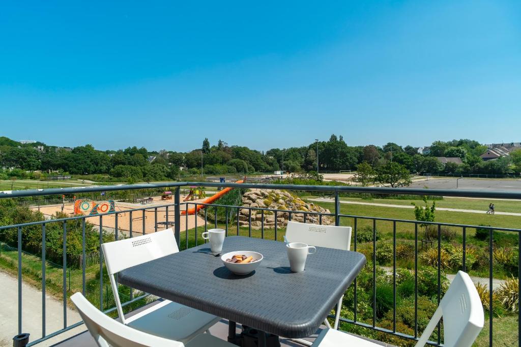 a table and chairs on a balcony with a view of a playground at Les Thermes 521 - Appt proche plage avec piscine partagée in Concarneau