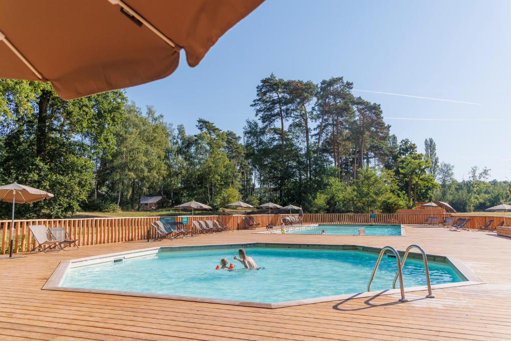 a swimming pool with two people in the water at Huttopia De Meinweg in Herkenbosch