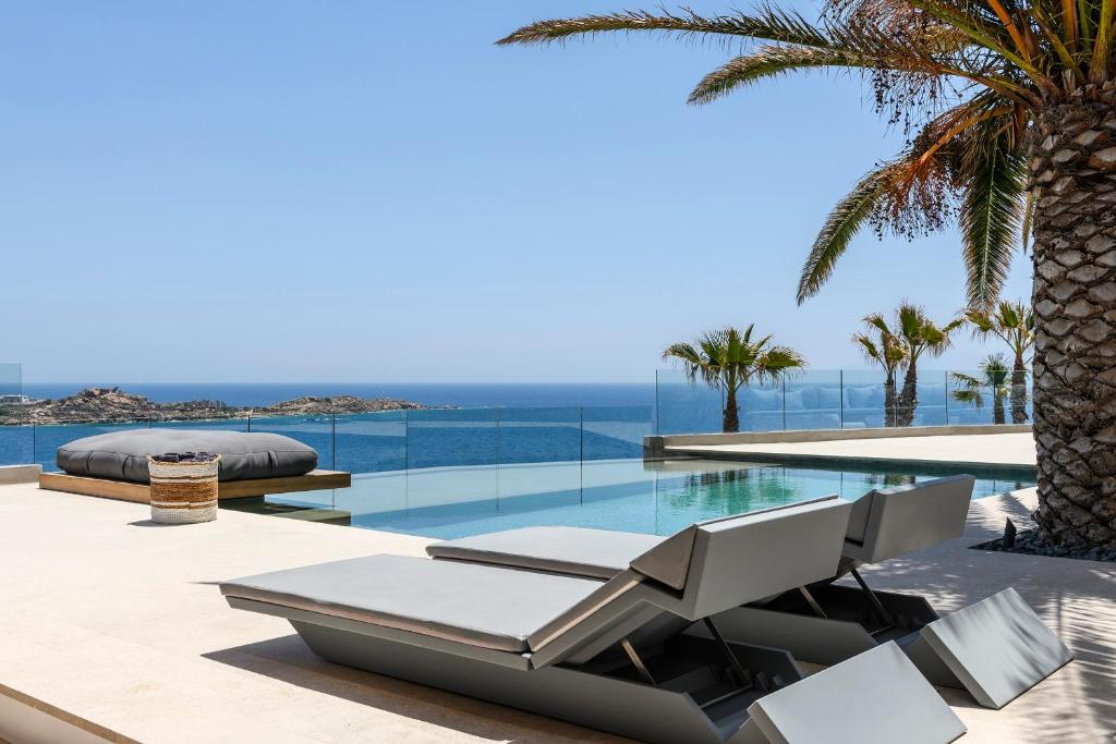 a pool with two lounge chairs and a palm tree at Villa Lilium II - Sanctuary overlooking Psarou Bay in Psarou