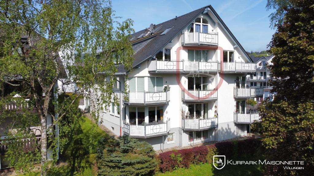a white apartment building with balconies and trees at Kurpark Maisonnette Willingen in Willingen