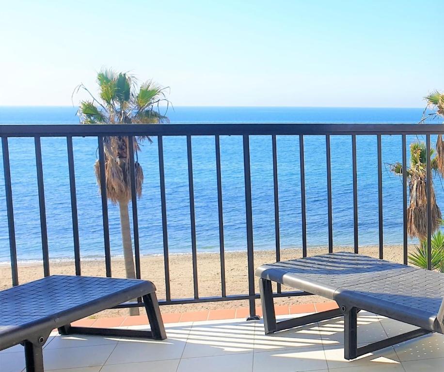een balkon met uitzicht op het strand met twee bankjes bij Sea Front Beach House Micaela I in Marbella